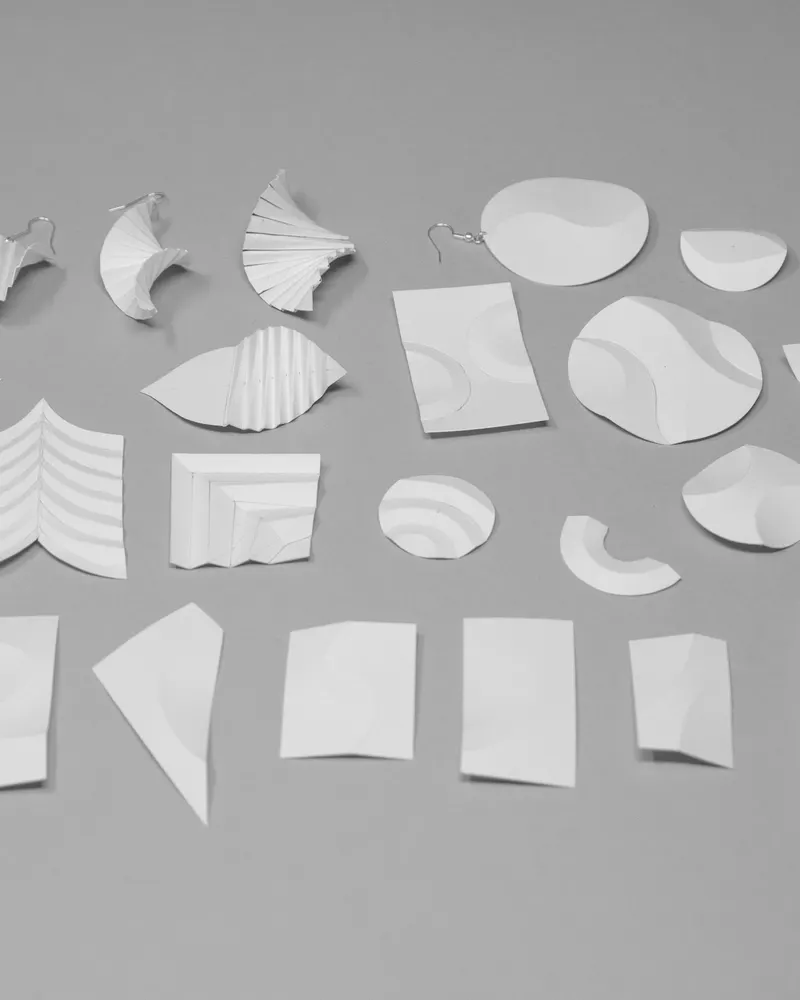Small white paper shapes, folded and cut, laid out in loose rows on a grey surface